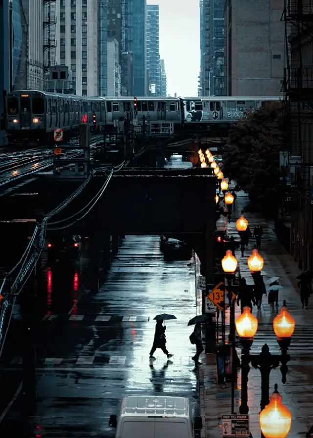 An L train passes over a rainy Chicago street lined with glowing lamps